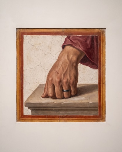 Primer plano de una mano con un anillo de hierro apoyada sobre piedra.